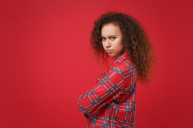 Side view of offended african american girl in pajamas homewear resting at home isolated on red background. Relax good mood lifestyle concept. Mock up copy space. Holding hands crossed looking camera.