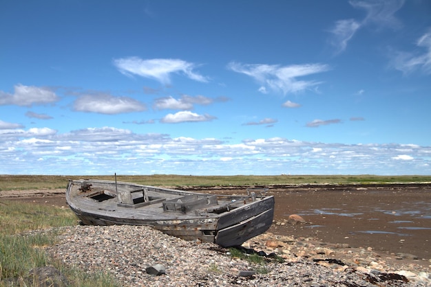 Вид сбоку на старую деревянную лодку, разбитую и застрявшую на пляже