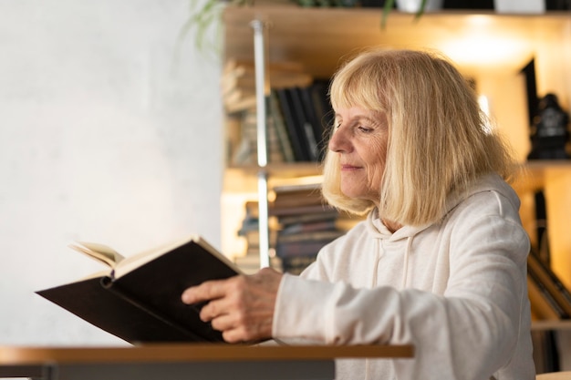 Foto vista laterale della donna anziana che legge un libro a casa