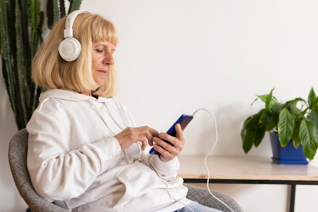 Foto vista laterale della donna anziana con le cuffie utilizzando lo smartphone