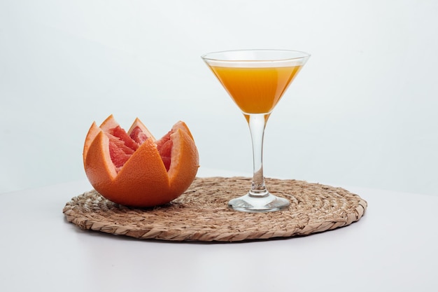 Side view of orange juice in glass and cut grapefruit on white background