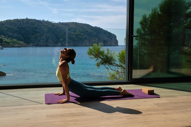 Side view of peaceful female in activewear stretching body while practicing yoga in Cobra pose on mat at home