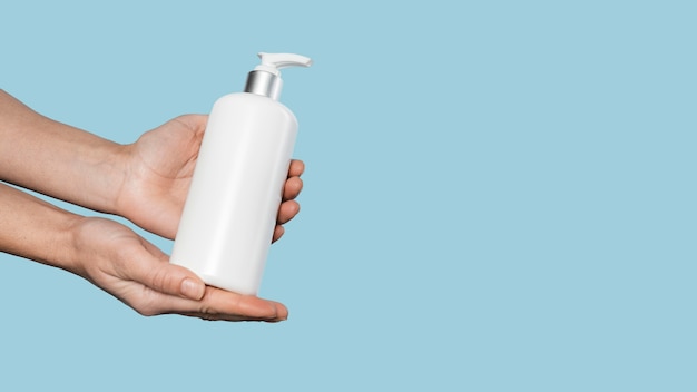 Photo side view person holding a bottle of liquid soap with copy space