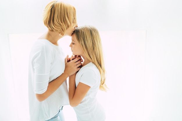 Side view photo of beautiful mother while she is kissing her little cute daughter