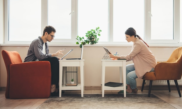 Side view photo of a caucasian business couple working from home at the computers and writing something near the window