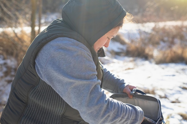 晴れた雪の日に外で暖かい服を着た旅行者の女性の側面写真は彼女のバッグを開けて...