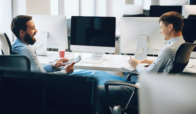 Foto di vista laterale di due uomini che hanno una discussione di lavoro nel loro ufficio mentre si utilizza un tablet