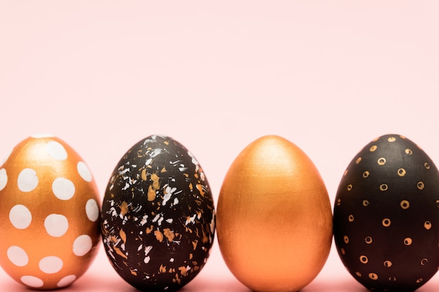 Side view of pink, white, black and golden decorated easter eggs in a row on pink background. Trendy holiday backdrop.