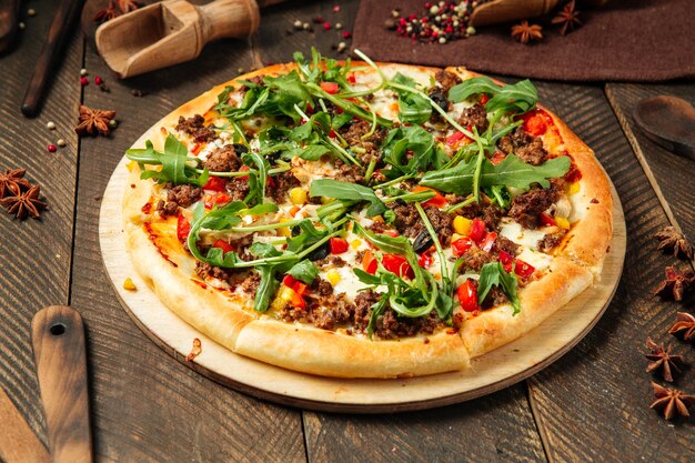 Side view on pizza with minced meat and arugula on the wooden table