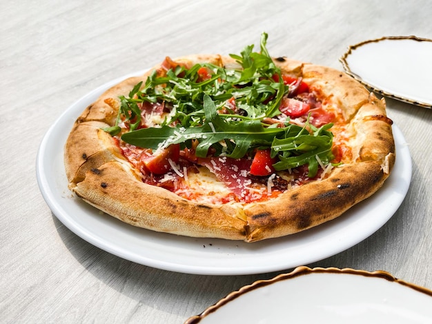 Side view of pizza with prosciutto arugula tomatoes and parmesan on a white plate on the table Italian cuisine Stand Dough Nutrition Menu Circle Small Slice Prosciutto Sauce Dish