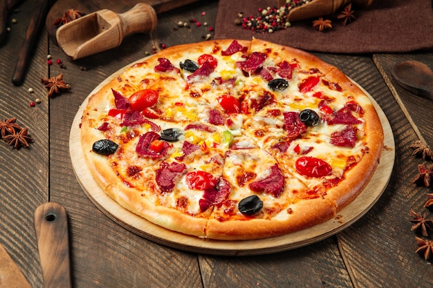 Vista laterale sulla pizza con carne affumicata e verdure sul tavolo di legno