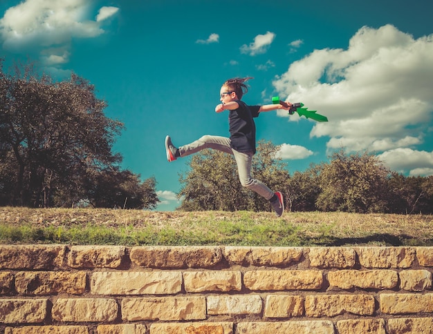 Photo side view of playful boy jumping over retaining wall