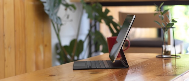 Side view of portable workspace with digital tablet, mug and plant vase decorated on wooden table