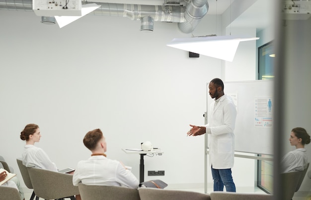 Side view portrait of African-American man standing by whiteboard while giving presentation during medical seminar in college, copy space