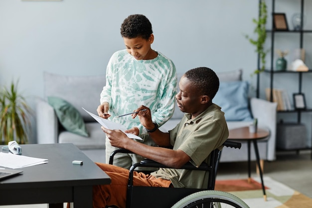 Side view portrait of african american man in wheelchair helping daughter with math problem for scho...