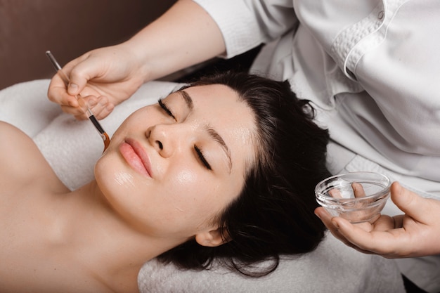 Side view portrait of a attractive woman leaning on a spa bed with closed eyes having a anti age mask with hyaluronic acid by a cosmetologist.