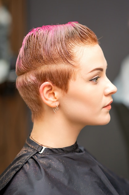 Ritratto di vista laterale di una bellissima giovane donna caucasica con un taglio di capelli rosa corto in attesa di un parrucchiere in un salone di bellezza