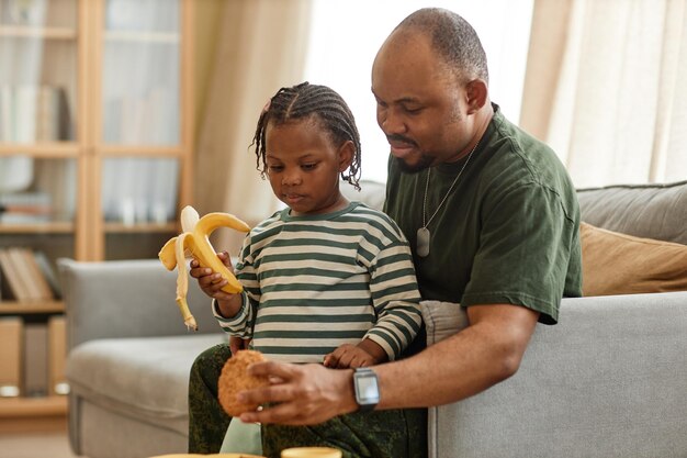 Side view portrait of black military dad sharing breakfast with\
cute daughter at home