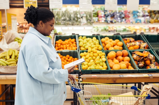 Side view portrait of black woman reading shopping list while buying groceries in supermarket copy s