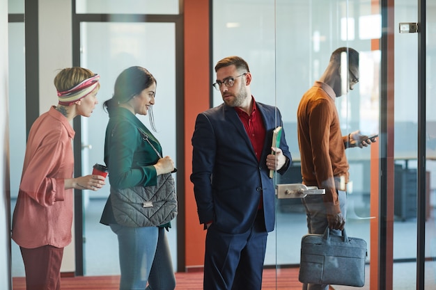 Side view portrait of business people standing in line in office, focus on mature bearded businessman talking to young woman, copy space