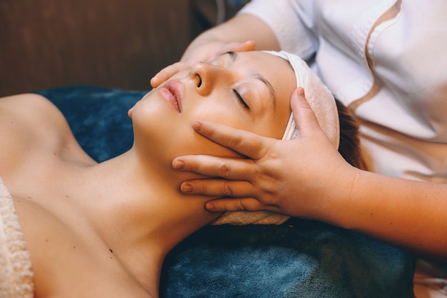 Side view portrait of a charming caucasian female leanin with closed eyes while having a relaxing facial massage in a spa salon.