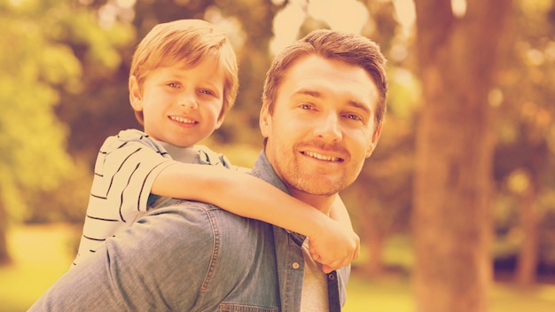 Photo side view portrait of a father carrying young boy on back at the park