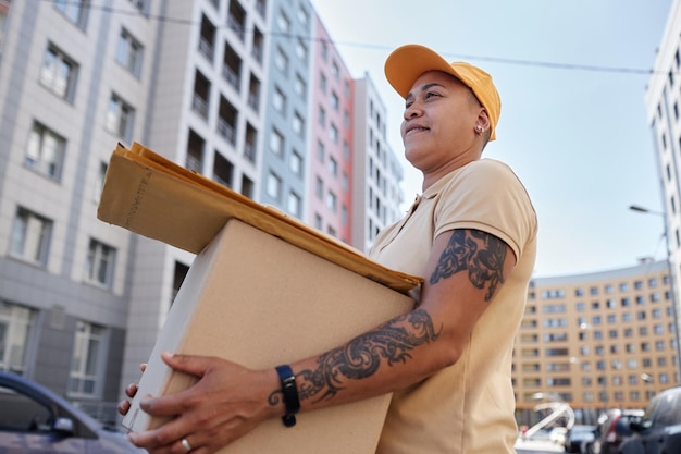 Side view portrait of female delivery worker holding box in city setting