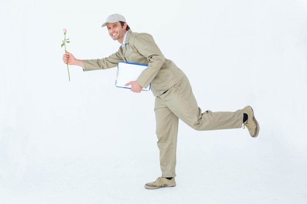 Side view portrait of happy delivery man with clipboard offering flower against white background