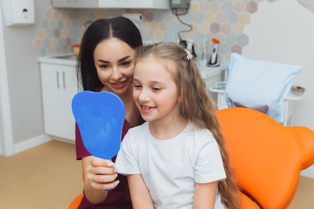 Ritratto di vista laterale della bambina che guarda lo specchio in odontoiatria pediatrica dopo chirurgia dentale