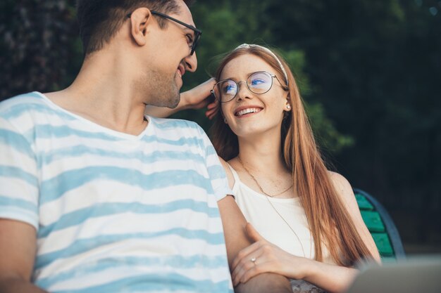 공원에서 수업 후 벤치에 앉아 웃고 그녀의 남자와 이야기 사랑스러운 빨간 머리 여자의 측면보기 초상화.