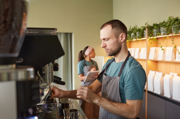 コーヒーマシン、コピースペースを操作しながらカフェで淹れたてのコーヒーを作る男性バリスタの側面図の肖像画