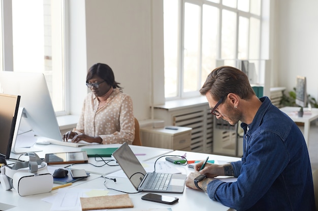 Side view portrait of male software engineer designing mobile
application or website while working with laptop in office, copy
space