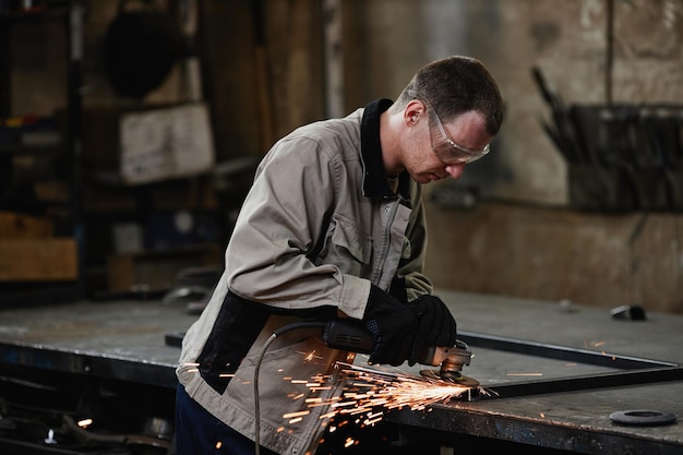 Side view portrait of male worker cutting metal with sparks flying in dark workshop copy space