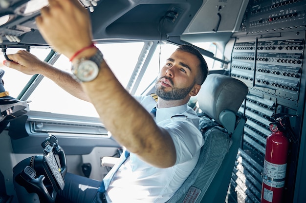 Side view portrait of man pilot in uniform pushing buttons in main cabin of passenger plane