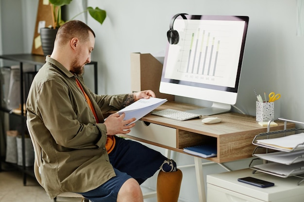 Side view portrait of man with prosthetic leg working at home\
office and reading documents copy spac