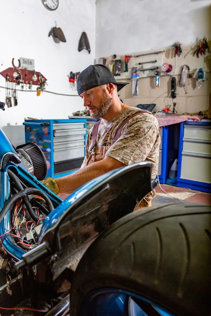 Photo side view portrait of man working in garage repairing motorcycle and customizing