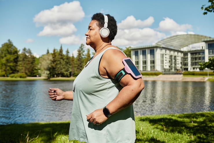 Photo side view portrait of mature black woman running outdoors and wearing headphones enjoying workout