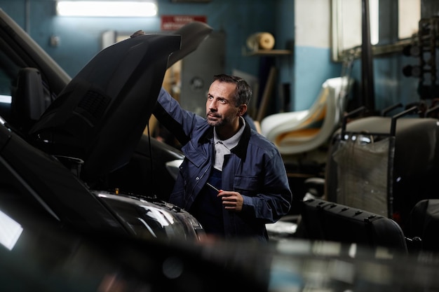 Photo side view portrait of mature car mechanic repairing trucks in garage with accent light copy space