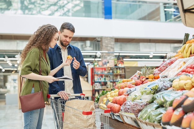 Side view portrait of modern young couple choosing vegetables while shopping for groceries at farmers market