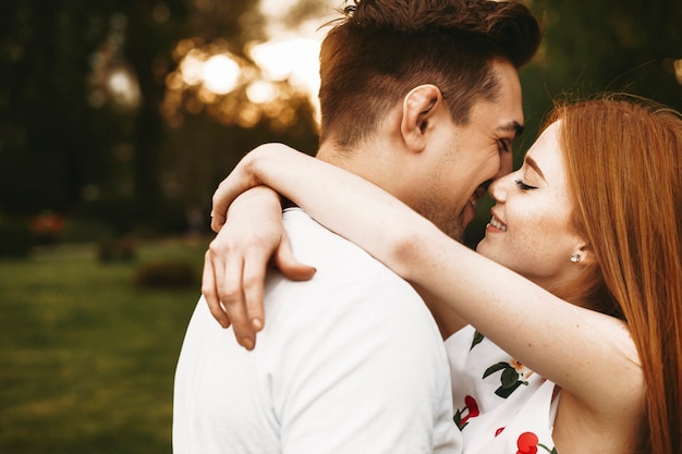Фото Портрет вид сбоку удивительной пары, обнимающейся и улыбающейся перед поцелуем с закрытыми глазами на фоне заката в городе.