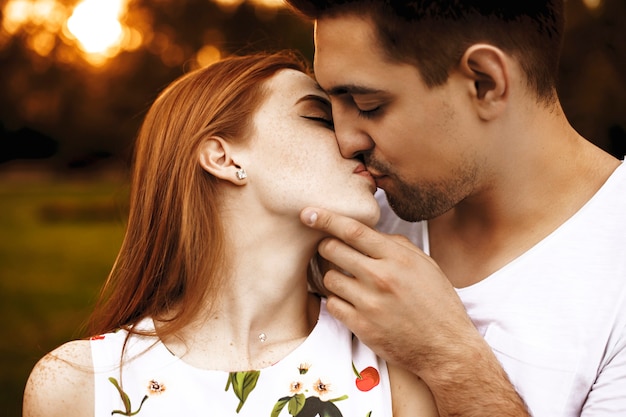 写真 男が彼のガールフレンドの顔に触れている間、目を閉じて日没に対してキスしている驚くべき若いカップルの側面図の肖像画。