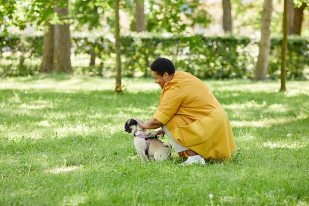 녹색 공원과 웃는 카피 공간에서 귀여운 개를 훈련시키는 성숙한 흑인 여성의 측면 초상화