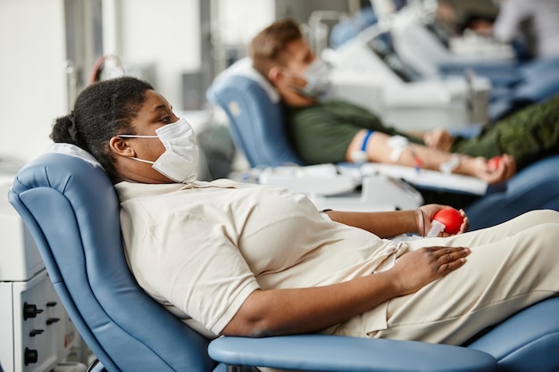 Side view portrait of people wearing masks while giving blood in row at medical donation center