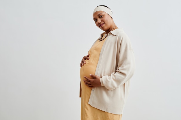 Side view portrait of pregnant African-American woman looking at camera while standing against white background, copy space