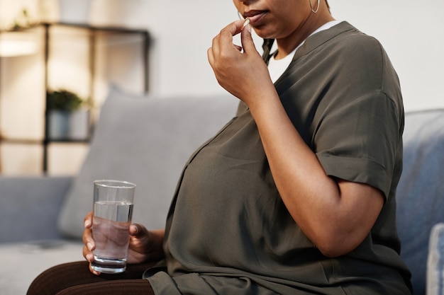 Ritratto di vista laterale della donna afroamericana incinta che prende le vitamine prenatali a casa, spazio della copia