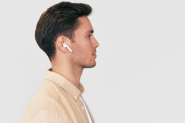 Side view portrait of serious young handsome man posing with wireless earphones on white studio background Caucasian businessman using wireless headphone