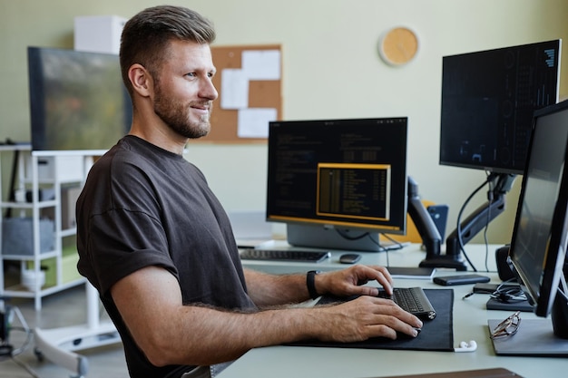 Side view portrait of smiling caucasian man as computer programmer writing code at office workplace