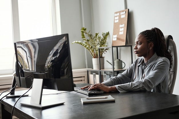 Ritratto in vista laterale di una donna afroamericana di successo che utilizza il computer mentre è seduto alla scrivania in ufficio, concetto di ceo femminile, spazio di copia