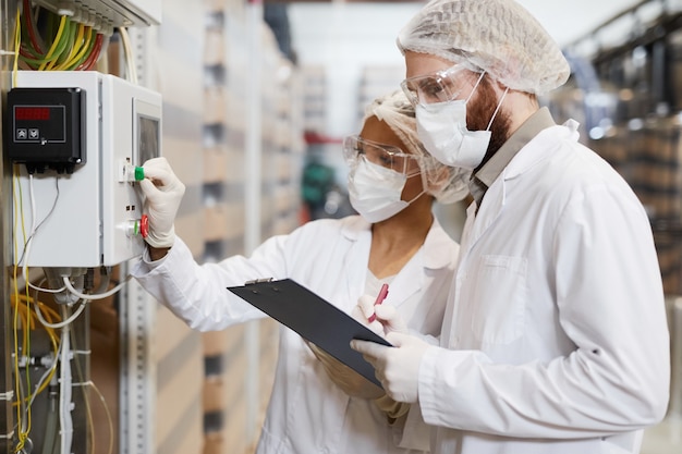 Вид сбоку портрет двух рабочих в защитной одежде во время работы с машинами на химическом заводе, копия пространства