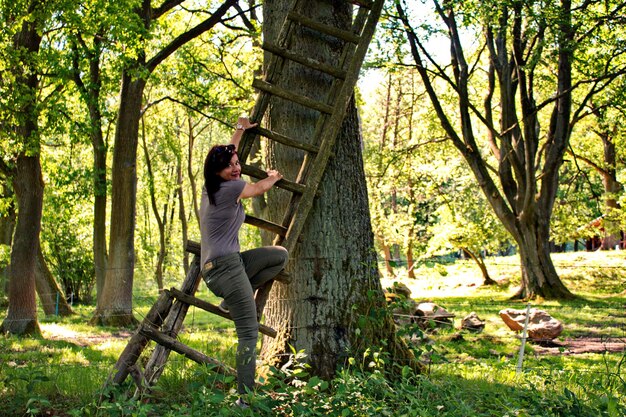 Foto ritratto di una donna che tiene in mano una scala dal tronco di un albero nella foresta